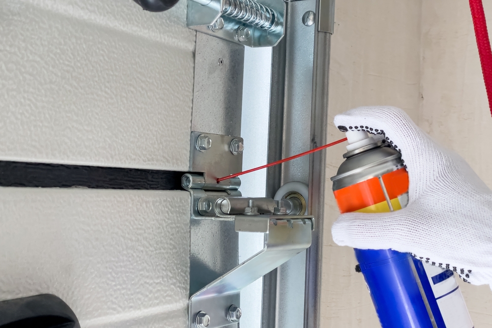 a garage door technician lubricates the hinge on a garage door during maintenance